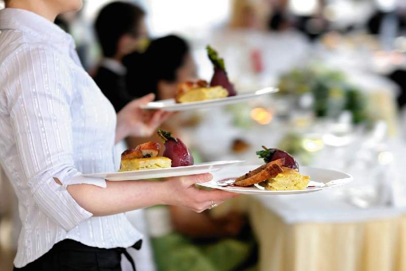 A person holding plates of food on top of a table.